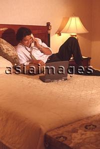 Asia Images Group - Male executive in hotel room talking on phone, with laptop computer