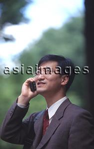 Asia Images Group - Male executive talking on cellular phone, trees behind