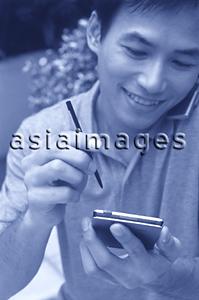 Asia Images Group - Man talking on cellular phone holding palmtop