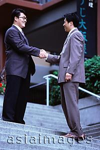 Asia Images Group - Two male executives shaking hands on stairway