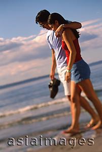 Asia Images Group - Young couple walking on beach, man with arm around woman's shoulder