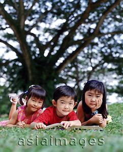 Asia Images Group - Three children lying down on grass reading a book