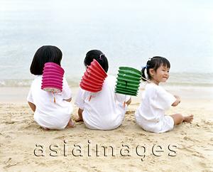 Asia Images Group - Three children sitting on the beach holding chinese lanterns, rear view