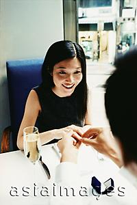 Asia Images Group - Man placing engagement ring on woman's finger in restaurant