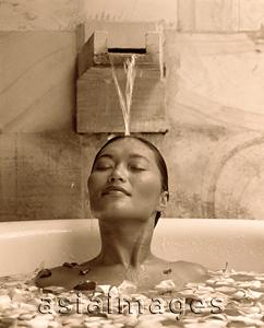 Asia Images Group - Woman relaxing in bathtub with flower petals, water pouring on head