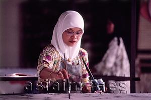 Asia Images Group - Malaysia, Kuala Terengganu, Muslim woman wearing tudung paints fabric at batik factory.