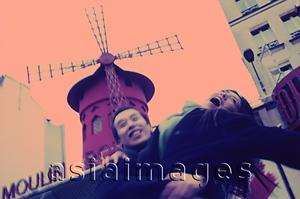 Asia Images Group - Man carrying woman, red windmill in background.