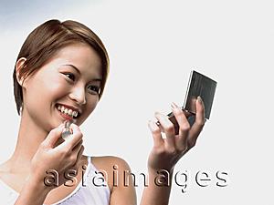 Asia Images Group - Woman applying lipstick, white background