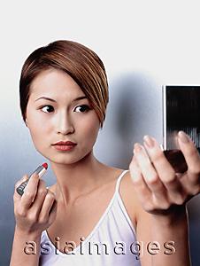Asia Images Group - Woman holding lipstick, looking in compact mirror