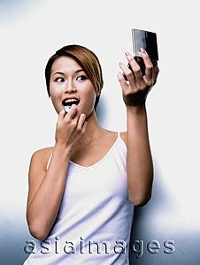 Asia Images Group - Woman applying lipstick, looking in compact mirror