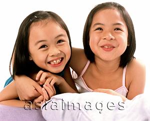 Asia Images Group - Two young girls embracing, laughing, white background.