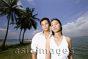 Asia Images Group - Young couple standing on beach, coconut trees in background, portrait