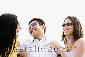 Asia Images Group - Man sitting between two woman, laughing, outdoors