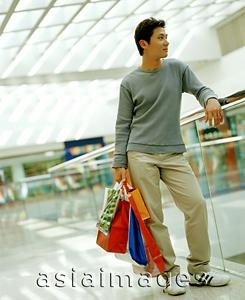 Asia Images Group - Casual dressed man holding shopping bags in mall leaning on railing.