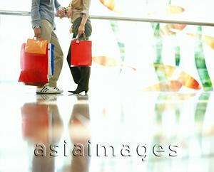 Asia Images Group - Lower body of couple holding shopping bags, talking and leaning on railing.