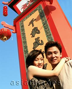 Asia Images Group - Couple embracing in front of chinese sign, lantern and blue sky in background.