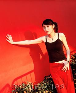 Asia Images Group - Young woman leaning on wall smiling, red background.