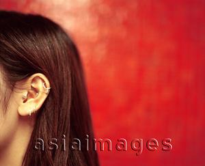 Asia Images Group - Profile of ear and hair of young woman, red background.