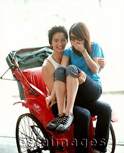 Asia Images Group - Young woman in sunglasses sitting on lap of man on rickshaw.