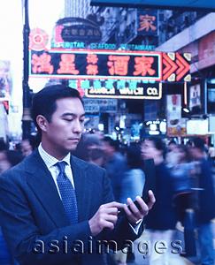 Asia Images Group - Male executive dialing cellular phone in busy street, neon lights in background.
