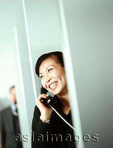 Asia Images Group - Woman executive using public telephone, male executive in background.