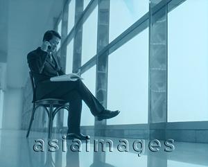 Asia Images Group - Executive sitting using cellular phone next to window.