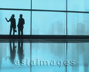 Asia Images Group - Silhouette of male and female executives by large window, skyline outside.