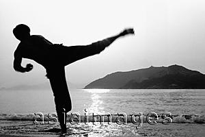 Asia Images Group - Man kicking in Kung Fu (Wu Shu) pose on beach, silhouette