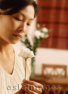 Asia Images Group - Woman looking at flower, dining room in background