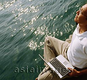 Asia Images Group - Man holding laptop, water in background