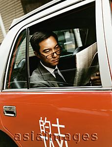 Asia Images Group - Executive wearing glasses reading newspaper in taxi.