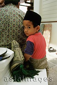 Asia Images Group - Malaysia, Malacca, Muslim boy with prayer rug nestles besides his father before Friday prayers at Kampong Kling Mosque.