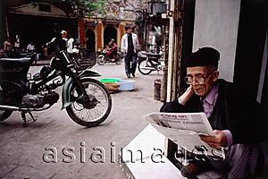 Asia Images Group - Vietnam, Hanoi, An elderly man sitting in a doorway reading a Vietnamese newspaper.
