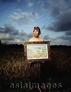 Asia Images Group - Indonesia, Bali, Ubud, Balinese artist holding painting in rice field.