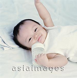 Asia Images Group - Baby girl, 9 months old holding milk bottle, smiling.