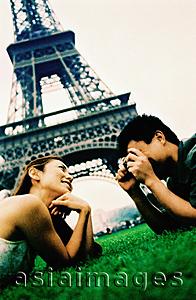 Asia Images Group - Young couple lying on grass, young woman posing for camera, smiling, Eiffel Tower in background. (high-grained)