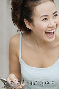 Asia Images Group - Young woman holding cellular phone, laughing