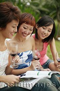 Asia Images Group - Young women browsing through magazine, wine glasses in hand
