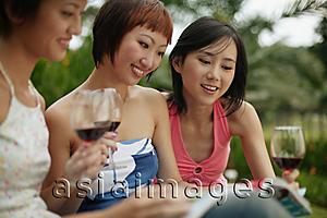 Asia Images Group - Young women browsing through magazine, wine glasses in hand