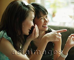 Asia Images Group - Young women whispering and pointing.