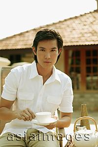 Asia Images Group - Young man holding cup and saucer, looking at camera