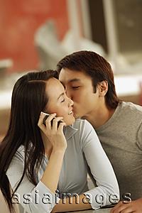 Asia Images Group - Young man kissing young woman, woman on the phone