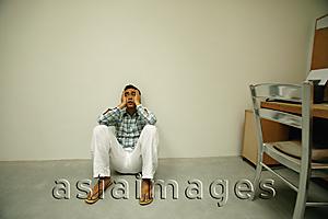 Asia Images Group - Man sitting on floor, hands on face, looking worried