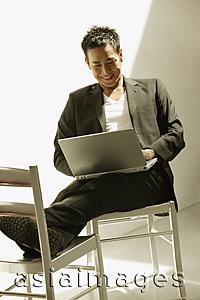 Asia Images Group - Man sitting down, using laptop, feet up on chair