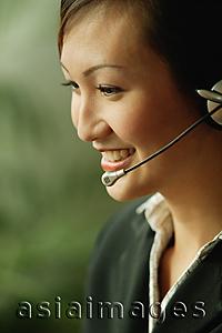 Asia Images Group - Young woman wearing hands-free device, side view