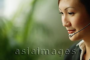 Asia Images Group - Young woman wearing hands-free device, looking down