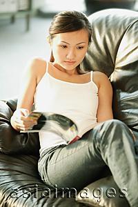 Asia Images Group - Young woman on sofa, looking at magazine