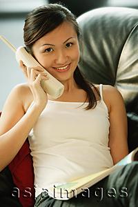 Asia Images Group - Young woman on sofa, holding telephone, smiling