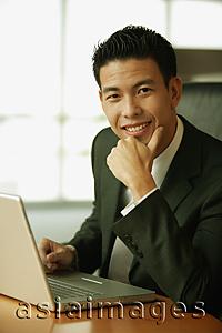 Asia Images Group - Young man with hand on chin, looking at camera, toothy smile