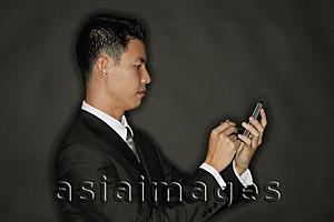 Asia Images Group - Young man using PDA, standing in profile